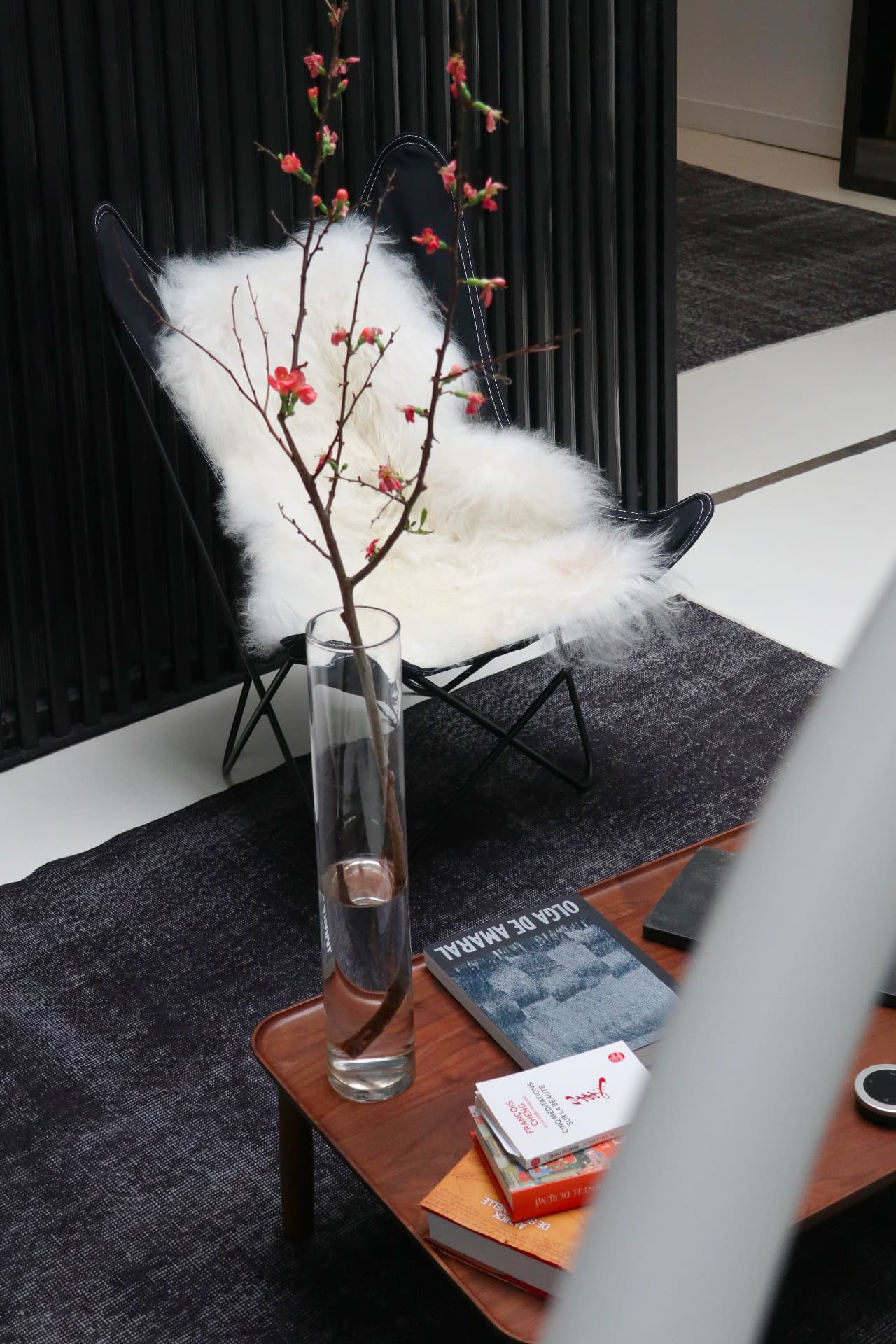 Fauteuil noir recouvert d'une fourrure blanche et branche fleurie dans un vase en verre